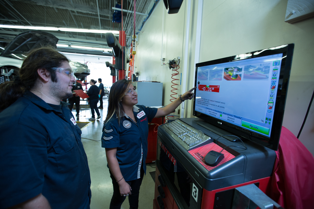 Instructor supervising a group of students as they work together to repair a car's engine in the automotive technology lab